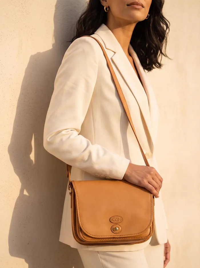 A woman in a cream blazer wearing a camel leather saddle crossbody in golden light